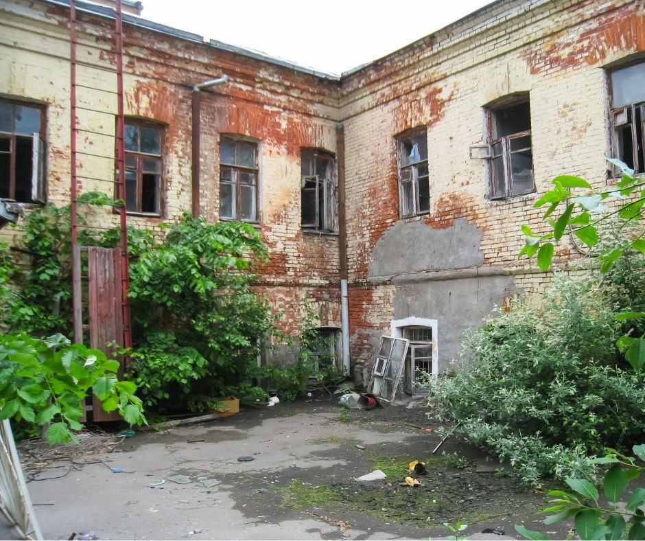 Façade d’un bâtiment ancien en briques dégradé, avec enduits décollés et fenêtres cassées, avant diagnostic et réhabilitation